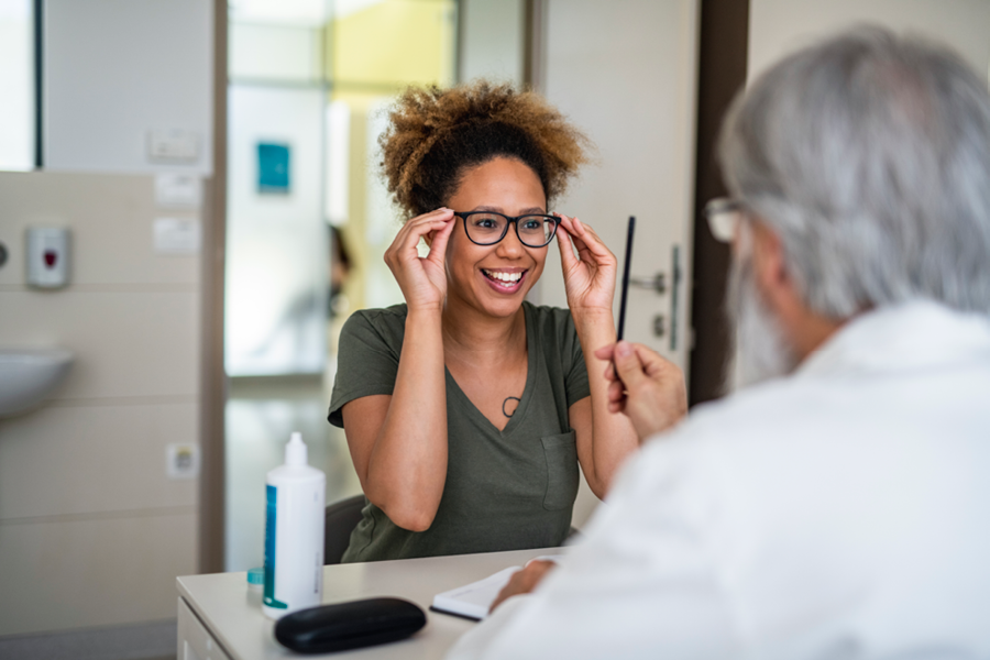 Person smiling and trying on glasses at the eye doctor.