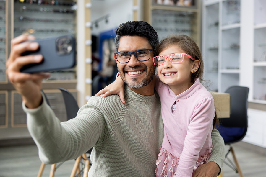 Father and daughter smiling and taking a selfie with their glasses on.