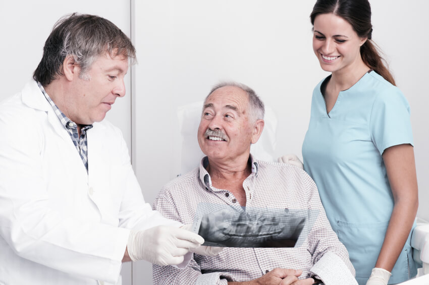 older man looking at dental x-rays with dentist and hygienist