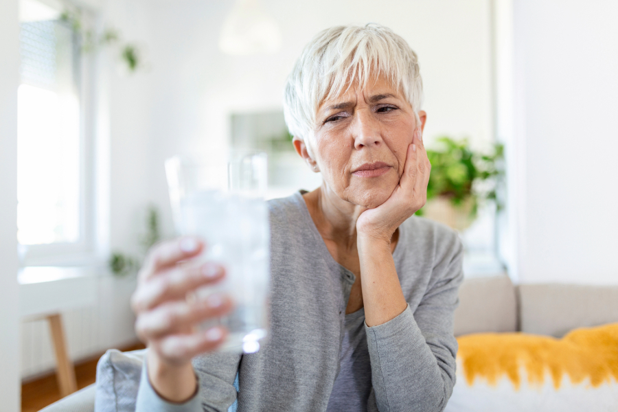 senior woman with sensitive tooth holding a glass of water